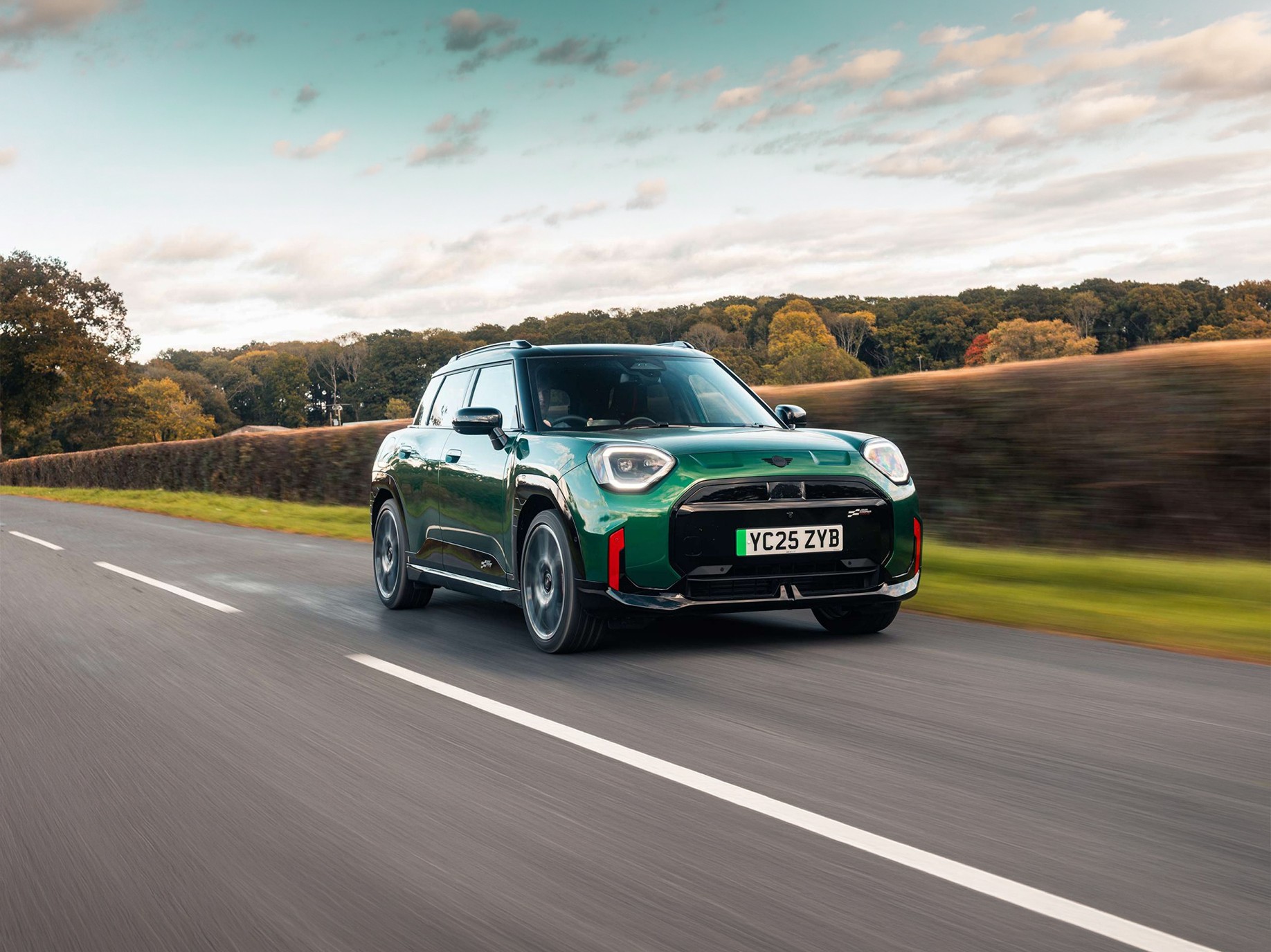 Front view of parking all-electric MINI Aceman in British Racing Green in car park with pink wall in the background